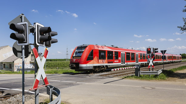 Ein roter Dieseltriebwagenzug vom Typ BR620 bei der Fahrt über einen Bahnübergang mit Andreaskreuzg und geschlossener Schranke.