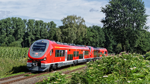 Ein roter Zug vom Typ Pesa Link fährt durch eine grüne Landschaft.
