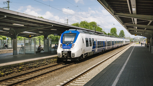 Ein weiß-blauer Zug vom Typ BR422 Talent2 fährt in einen Bahnhof ein.