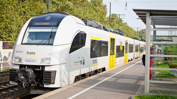 Ein weiß-gelber Zug vom Typ BR460 Desiro steht an einem Bahngleis.