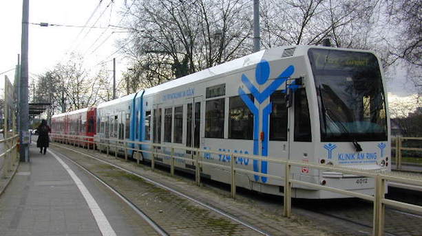 Ein weiß-blauer Niederflurstadtbahnwagen vom Typ K4000 steht an einer Haltestelle.