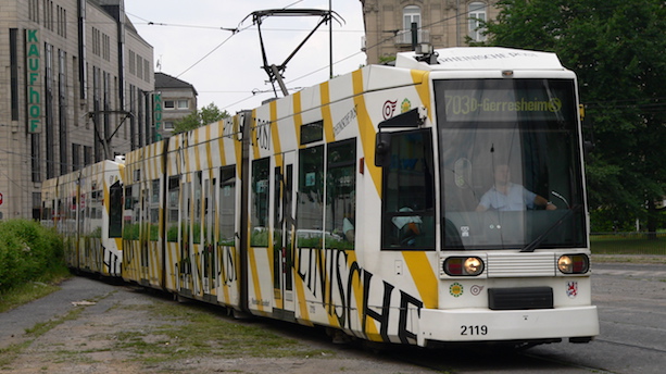 Ein weiß-gelb gestalteter Niederflurstraßenbahnwagen vom Typ NF6GT fährt über Straßenbahngleise.