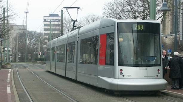 Ein silberner Niederflurstraßenbahnwagen vom Typ NF8 steht an einem Bahnsteig.