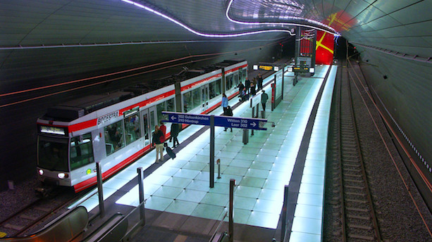 Ein weiß-roter Stadtbahnwagen vom Typ NF6D steht am Bahnsteig in einem modern gestalteten und beleuchteten U-Bahnhof.