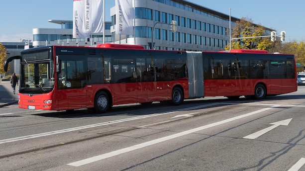 Ein roter Gelenkbus der Marke MAN biegt über eine Straßenkreuzung.