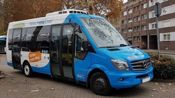 Ein blau-weißer Kleinbus steht auf einem Platz.