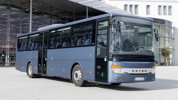 Ein Grauer Standardlinienbus für den Überlandverkehr steht auf einem Platz vor einem Gebäude mit Glasfront.