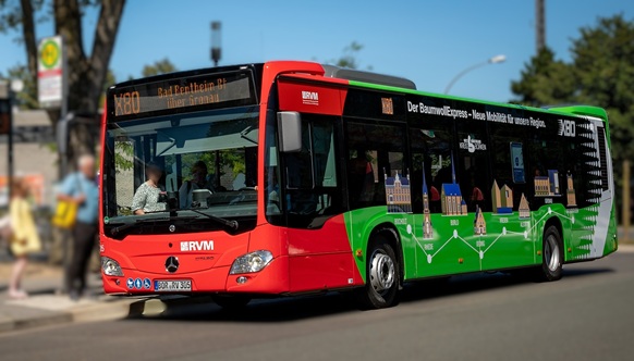Ein rot-grüner Standardlinienbus für den Überlandverkehr (Linie X80 der RVM) steht an einer Haltestelle.