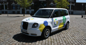 Das weiße On-Demand Fahrzeug G-Mobil der Stadt Gronau mit gelb-blau-grünem Logo und Akzenten