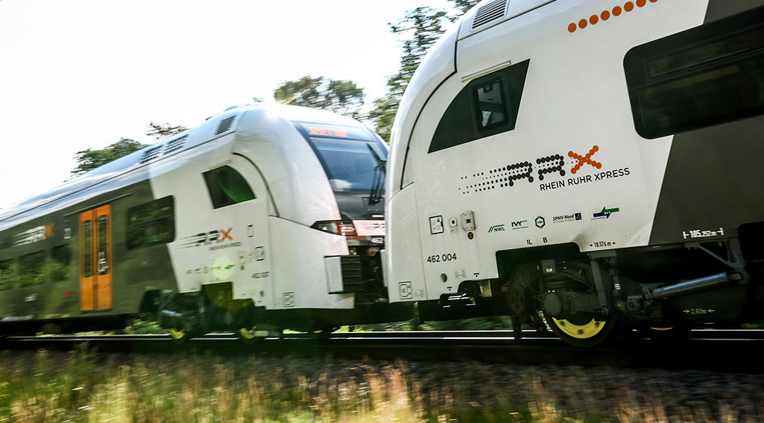 Ein Zug des Rhein-Ruhr-Express mit zwei Zugteilen fährt durch eine grüne Landschaft.