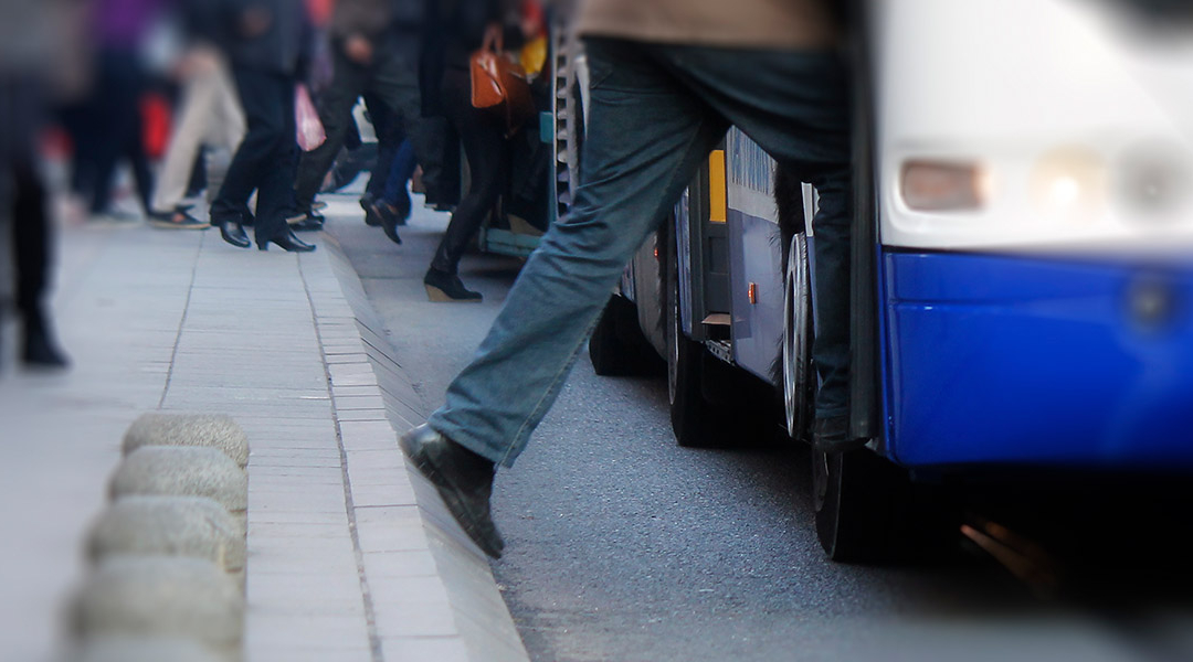 Menschen steigen von einer Bordsteinkante in einen Bus, nur die Beine sichtbar.