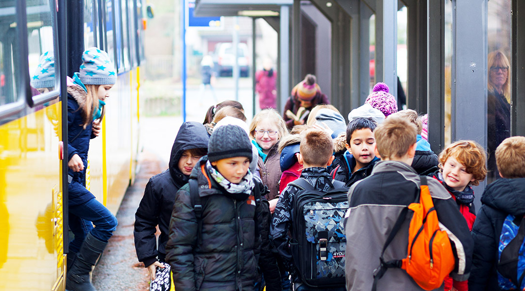 Eine Gruppe Schulkinder steht an einer Straßenbahnhaltestelle neben einer gelben Straßenbahn.