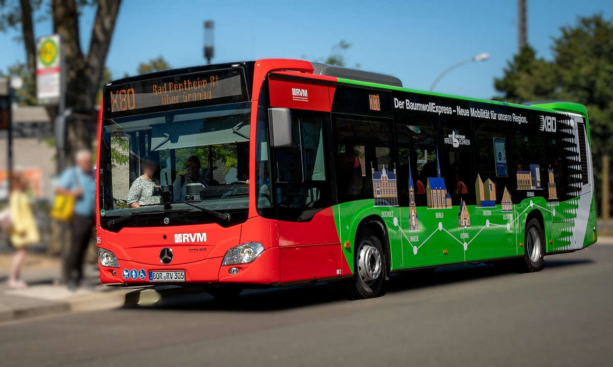 Ein rot-grüner Standardlinienbus für den Überlandverkehr (Linie X80 der RVM) steht an einer Haltestelle.