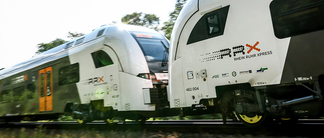 Ein Zug des Rhein-Ruhr-Express mit zwei Zugteilen fährt durch eine grüne Landschaft.