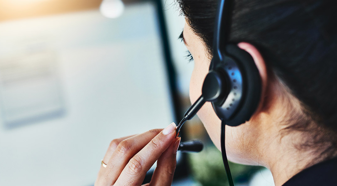 Blick über die Schulter einer Frau mit Headset auf einen verschwommen dargestellten Bildschirm