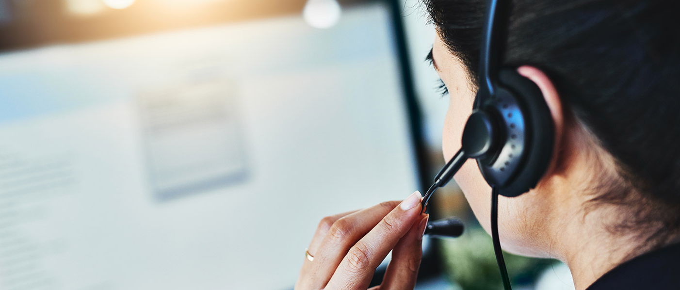 Blick über die Schulter einer Frau mit Headset auf einen verschwommen dargestellten Bildschirm