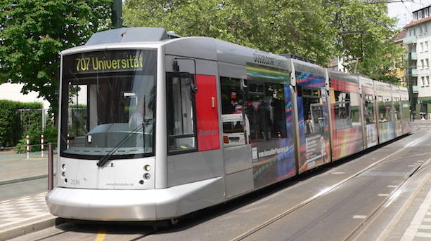 Ein silberner Niederflurstraßenbahnwagen vom Typ NF10 steht an einem Bahnsteig.